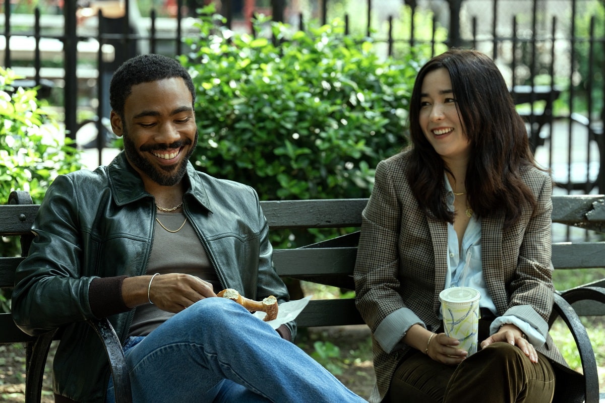 Donald Glover y Maya Erskine sentados en un banco en una plaza