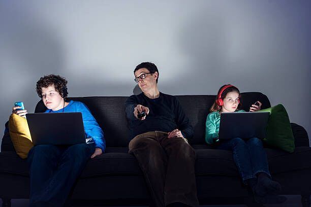 Dos hijos en edad escolar en sus laptops y su padre en medio de ellos.